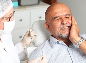 man in dental chair in pain holding cheek